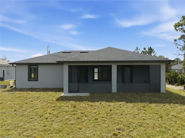 Back of house featuring a yard, a sunroom, roof with shingles, and stucco siding
