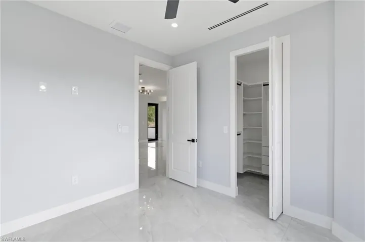 Unfurnished bedroom featuring a walk in closet, recessed lighting, ceiling fan, and light marble finish floors