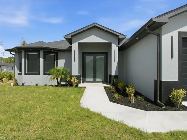 View of exterior entry with stucco siding, french doors, and a yard