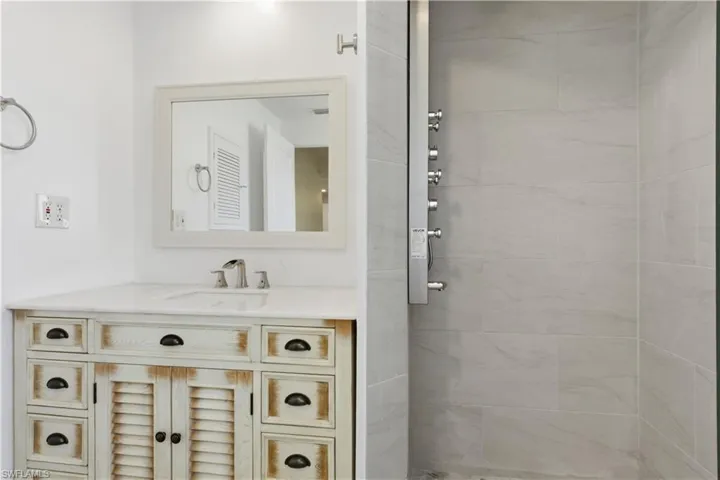 Distressed wood vanity with a white countertop and integrated sink, accompanied by a frameless mirror