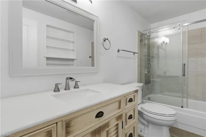 Vanity with a white countertop and undermount sink, brushed nickel faucet, framed mirror, and wood-finish cabinetry featuring dark hardware