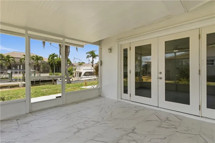 Screened lanai featuring large format tile flooring, white frame french doors, and water frontage