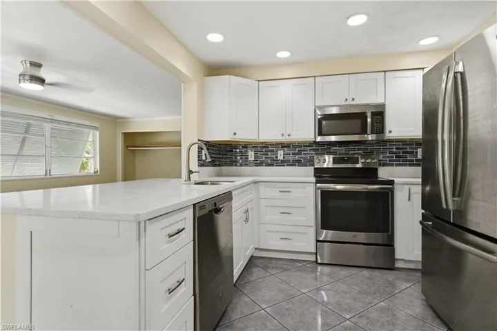 Kitchen featuring white cabinetry, stainless steel appliances, a tiled backsplash, and light countertops