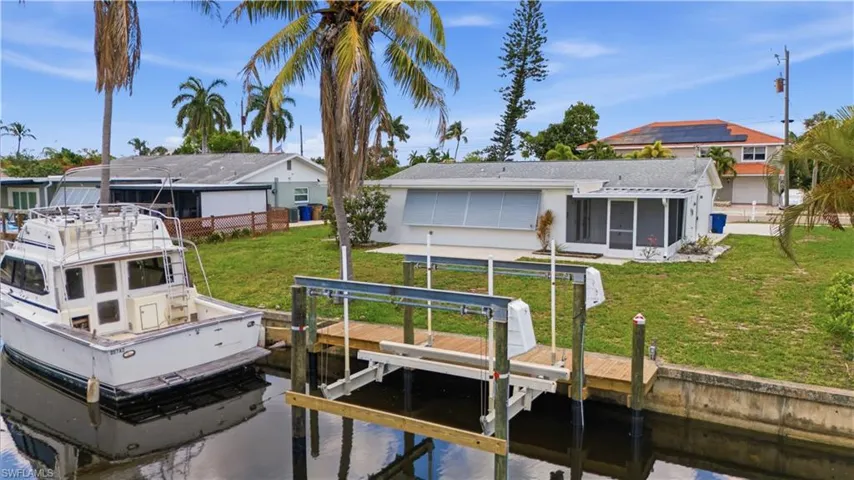 Waterfront property featuring a private boat lift, a screen-enclosed porch, and a manicured lawn