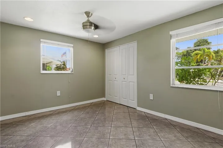 Interior room featuring tile flooring, neutral wall tones, two windows with white blinds, a ceiling fan with light fixture, and bi-fold closet doors