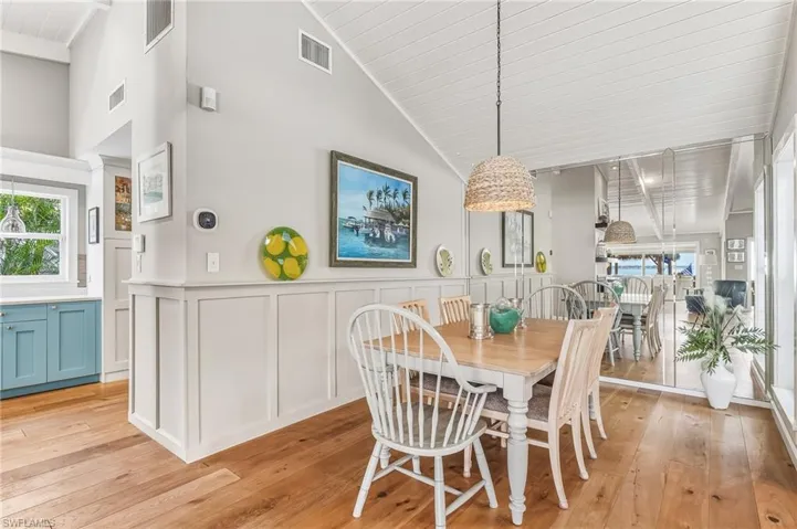 Dining area with a decorative wall, a wainscoted wall, light wood-type flooring, and high vaulted ceiling