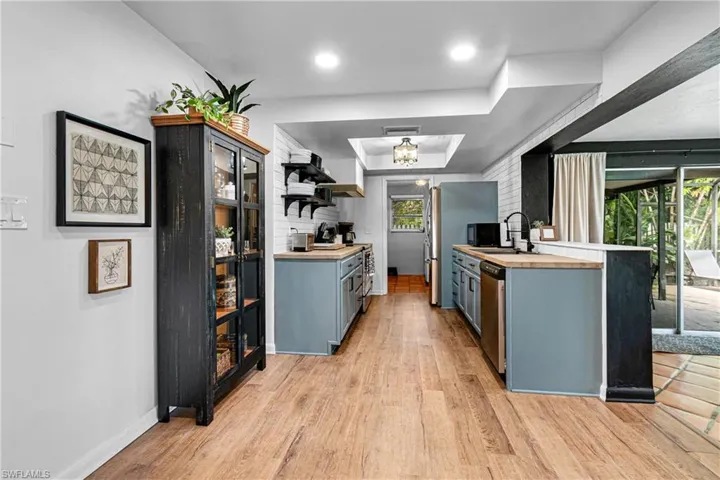 Kitchen featuring dishwasher, a tray ceiling, sink, butcher block counters, and light hardwood / wood-style flooring
