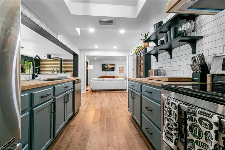 Kitchen featuring backsplash, stainless steel appliances, wooden counters, light wood-type flooring, and extractor fan