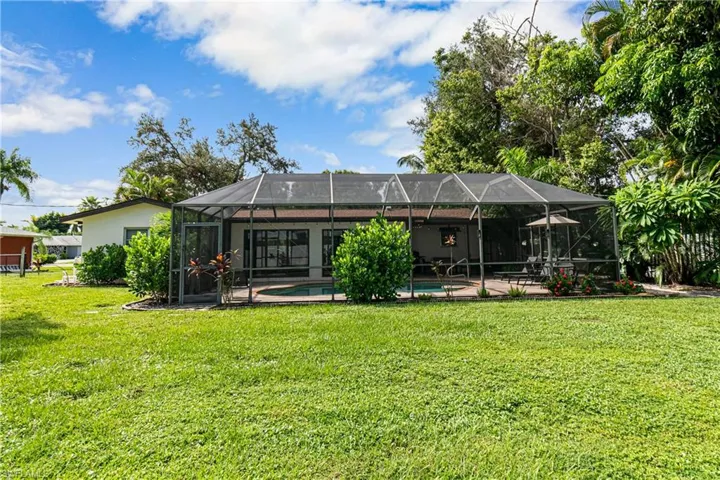 Rear view of property with glass enclosure, a patio, and a lawn