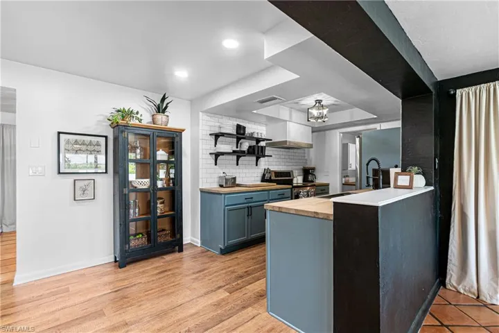 Kitchen with blue cabinets, tasteful backsplash, butcher block countertops, light hardwood / wood-style flooring, and stainless steel range