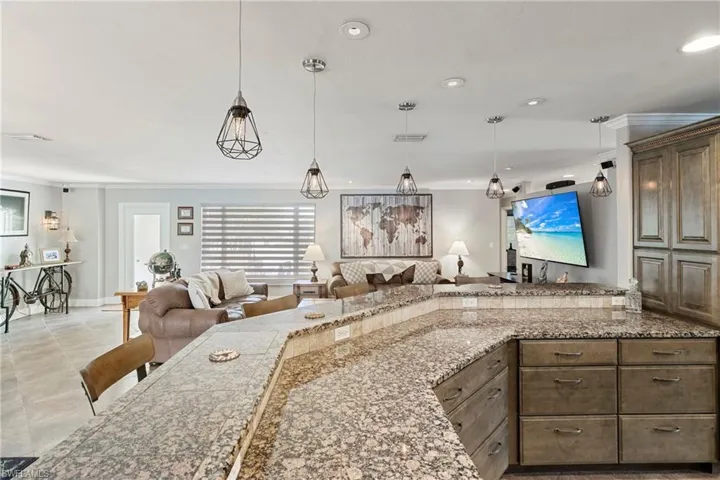Kitchen with open floor plan, ornamental molding, light stone countertops, decorative light fixtures, and recessed lighting