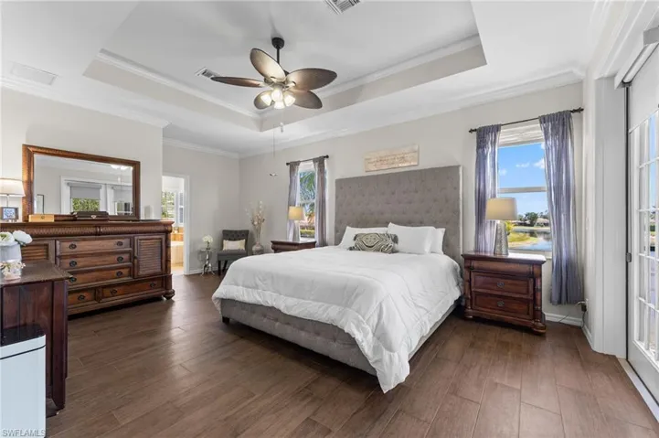 Primary Bedroom with tile wood like flooring, tray ceiling and french doors to screened balcony with pond and pool views.