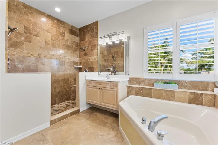 Tiled Primary Bathroom with corner tub, large walk-in shower and split vanities and walk-in closet