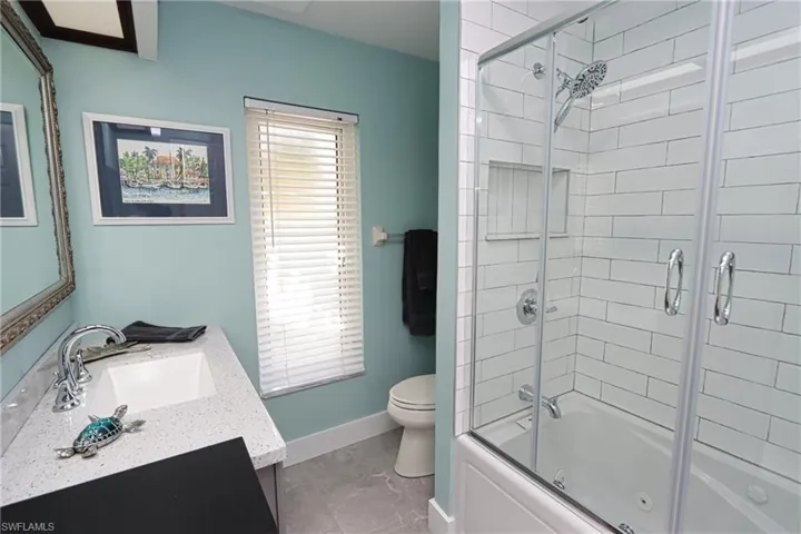 Full bathroom with tile flooring, vanity with extensive cabinet space, combined bath / shower with glass door, and toilet
