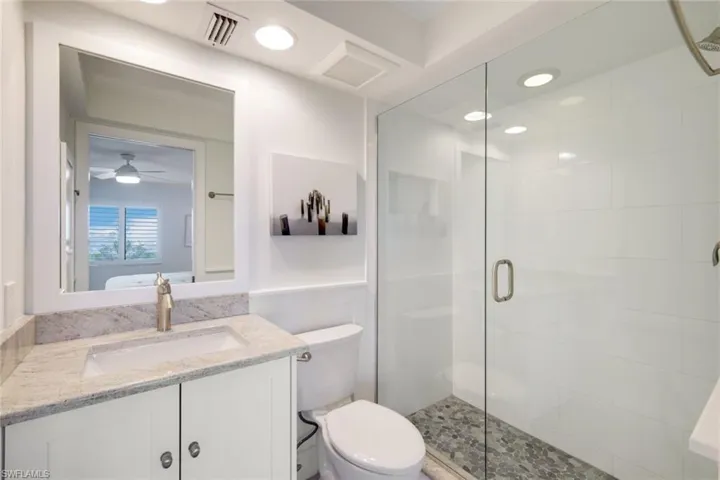 Bathroom with an enclosed shower, vanity, toilet, and ceiling fan