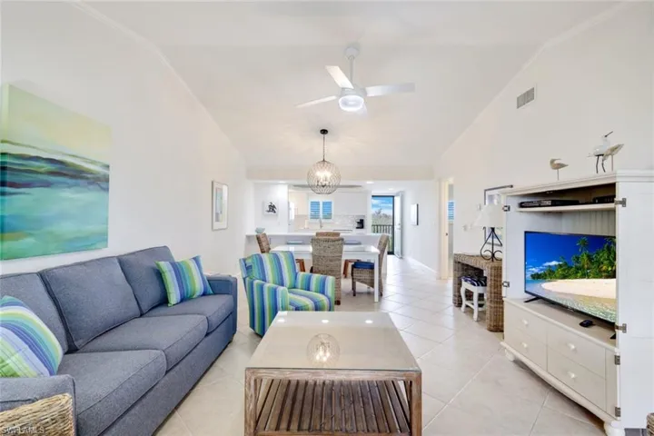 Living room with ceiling fan with notable chandelier, light tile patterned flooring, and vaulted ceiling