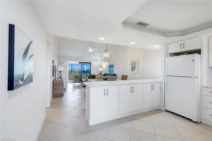 Kitchen featuring kitchen peninsula, white fridge, white cabinetry, and light tile patterned flooring