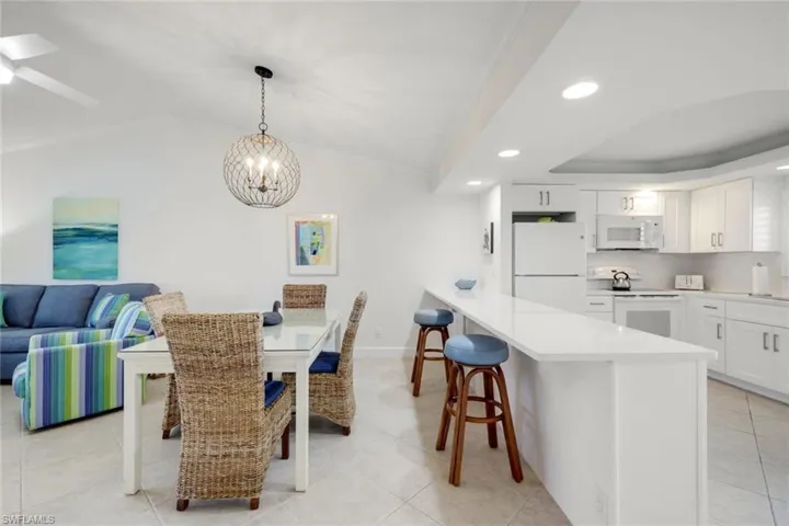 Dining room with ceiling fan with notable chandelier, lofted ceiling, and light tile patterned floors