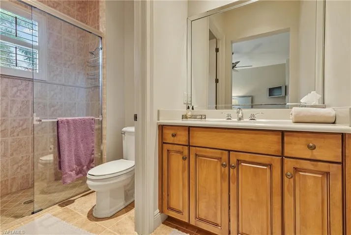 Bathroom with tile patterned flooring, a shower with shower door, ceiling fan, vanity, and toilet