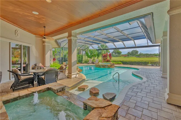 View of pool with pool water feature, glass enclosure, an in ground hot tub, and a patio area