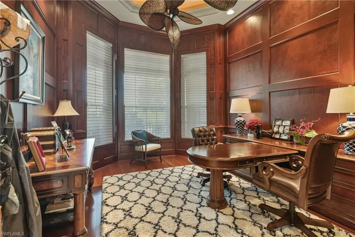 Office space with ornamental molding, wood walls, ceiling fan, and dark hardwood / wood-style floors