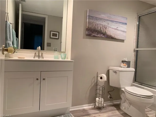 Updated guest bathroom featuring vanity, wood-type flooring, combined bath / shower with glass door, and toilet