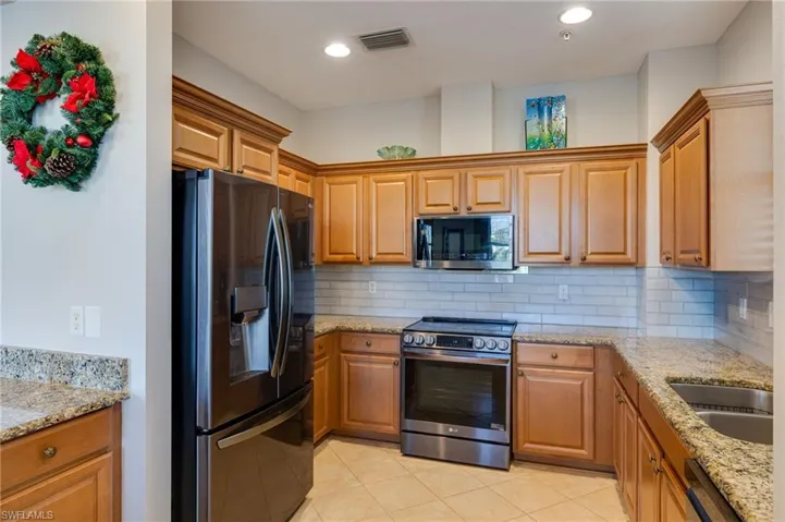 Kitchen with light stone countertops, appliances with stainless steel finishes, backsplash, brown cabinetry, and light tile patterned flooring