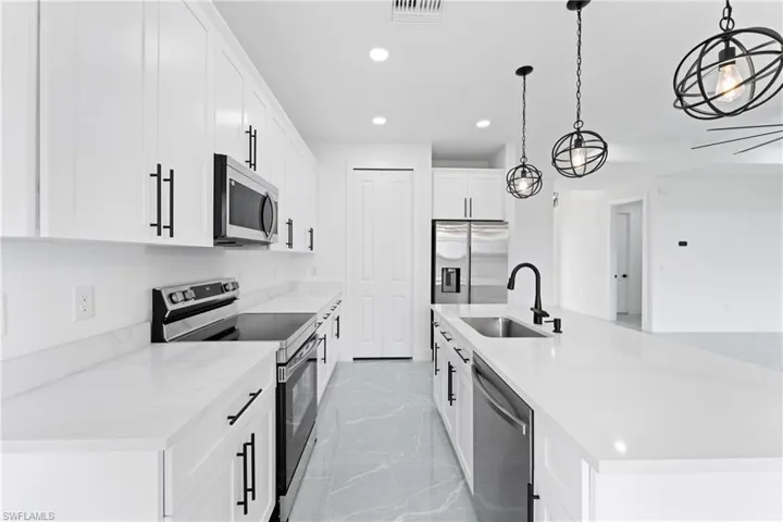 Kitchen featuring a kitchen island with sink, sink, appliances with stainless steel finishes, decorative light fixtures, and white cabinetry