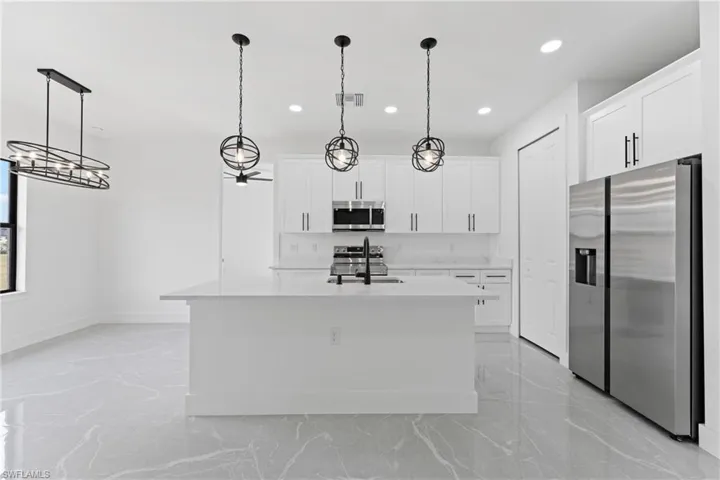 Kitchen featuring white cabinets, appliances with stainless steel finishes, hanging light fixtures, and an island with sink