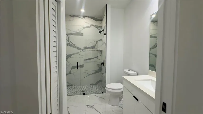 Bathroom featuring a tile shower, toilet, tile floors, and large vanity