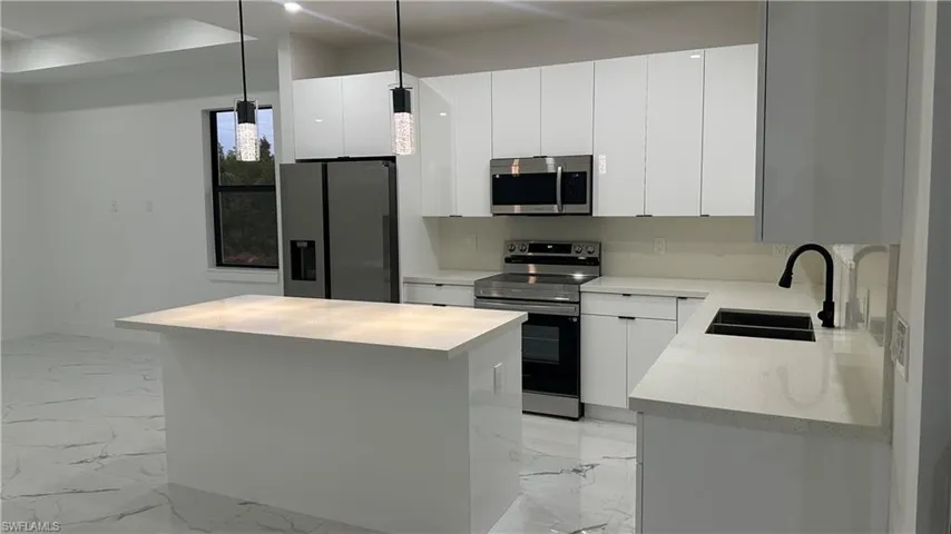 Kitchen with hanging light fixtures, sink, light tile floors, and appliances with stainless steel finishes