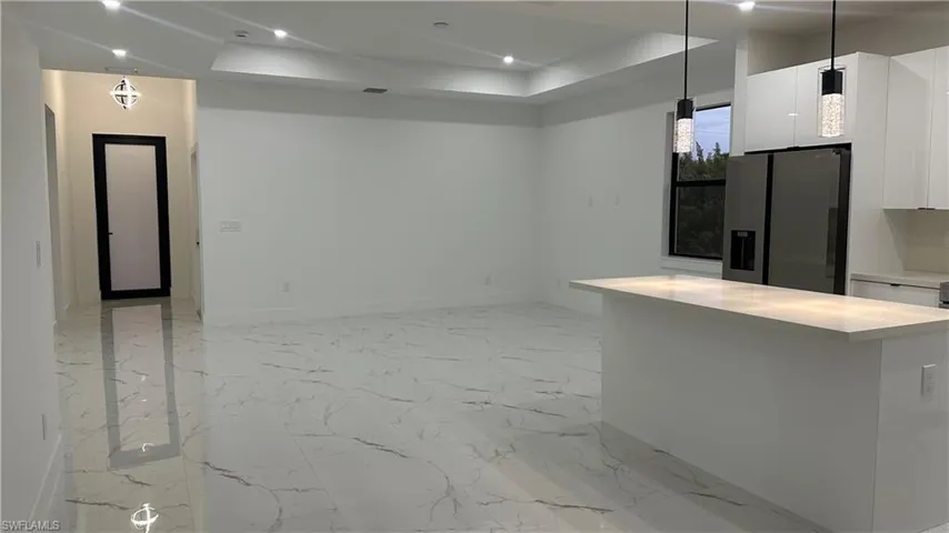 Kitchen with stainless steel refrigerator with ice dispenser, a raised ceiling, white cabinetry, and light tile floors