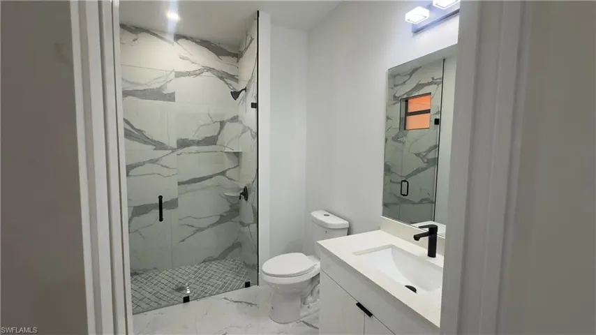 Bathroom with tile floors, a shower with shower door, toilet, and vanity
