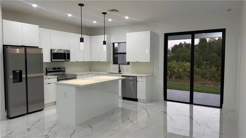 Kitchen featuring a center island, decorative light fixtures, white cabinetry, and stainless steel appliances