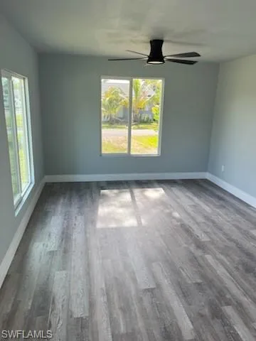 Unfurnished room featuring a wealth of natural light, ceiling fan, and dark wood-type flooring
