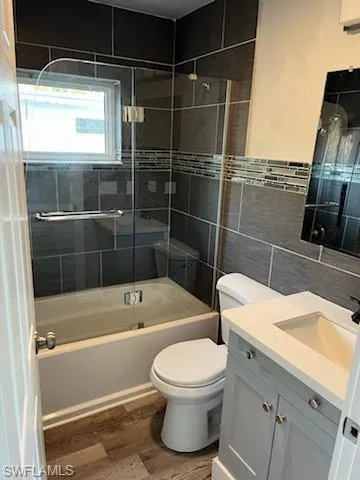 Full bathroom featuring vanity, tiled shower / bath combo, toilet, tile walls, and wood-type flooring