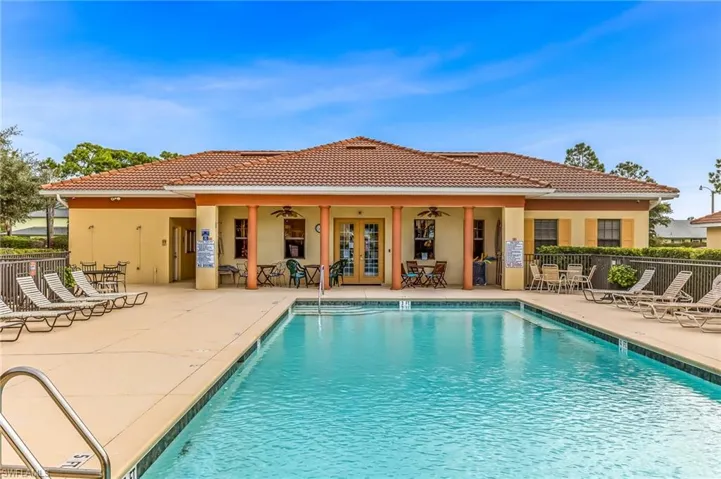 Expansive outdoor pool area featuring a rectangular swimming pool, concrete decking, and a stucco-finished building with a terracotta tile roof and columned patio