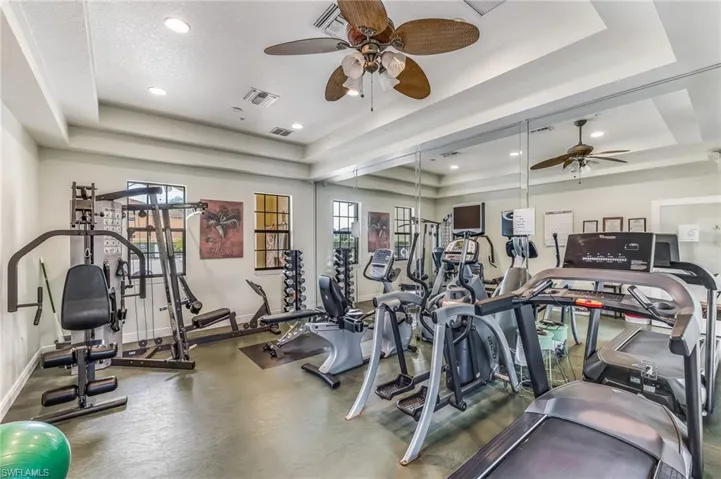 Fitness center with multiple exercise machines, mirrored wall, tray ceiling, recessed lighting, and ceiling fans