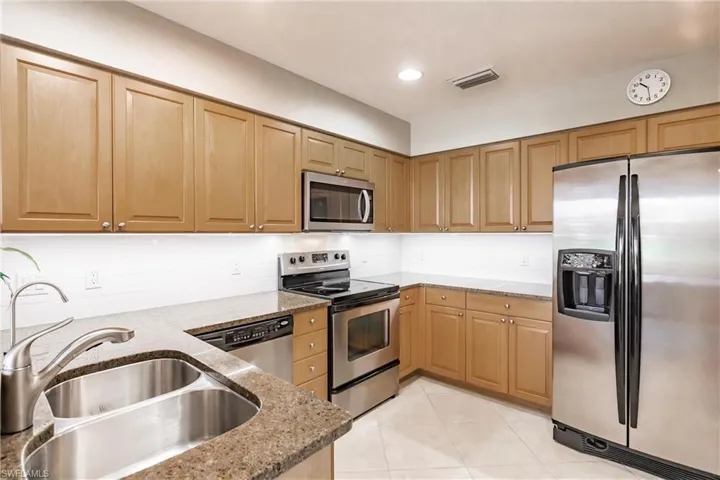 Kitchen with sink, decorative backsplash, light tile patterned flooring, light stone counters, and stainless steel appliances