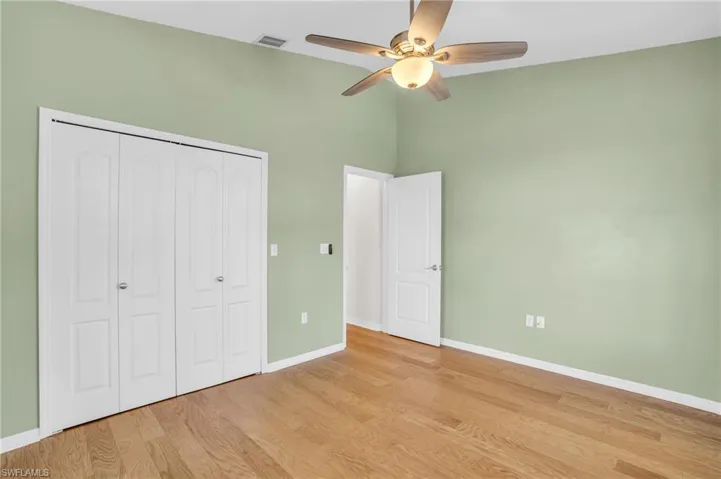 Unfurnished bedroom with a closet, ceiling fan, light hardwood / wood-style floors, and a towering ceiling