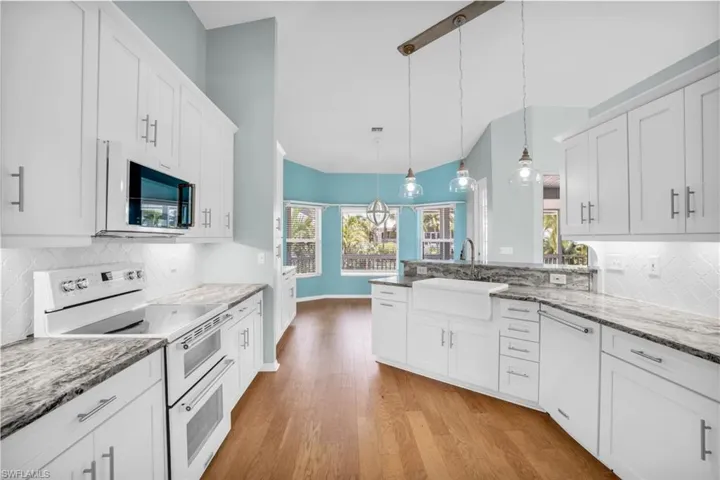 Kitchen with decorative light fixtures, white cabinetry, white appliances, light hardwood / wood-style floors, and backsplash
