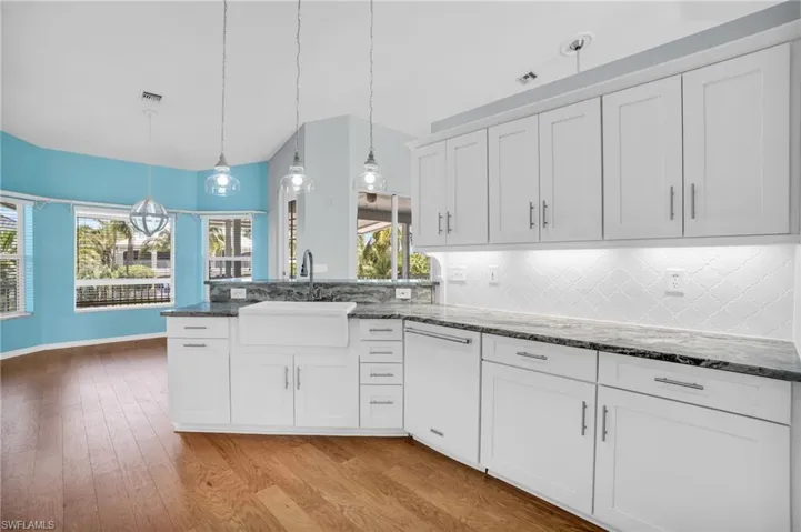 Kitchen with lofted ceiling, hardwood / wood-style floors, decorative backsplash, decorative light fixtures, and sink