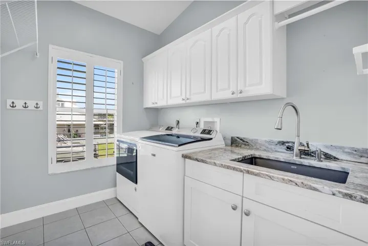 Clothes washing area featuring light tile patterned flooring, independent washer and dryer, sink, and cabinets