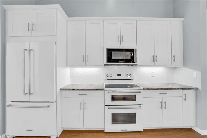 Kitchen featuring white appliances, decorative backsplash, light wood-type flooring, stone countertops, and white cabinetry