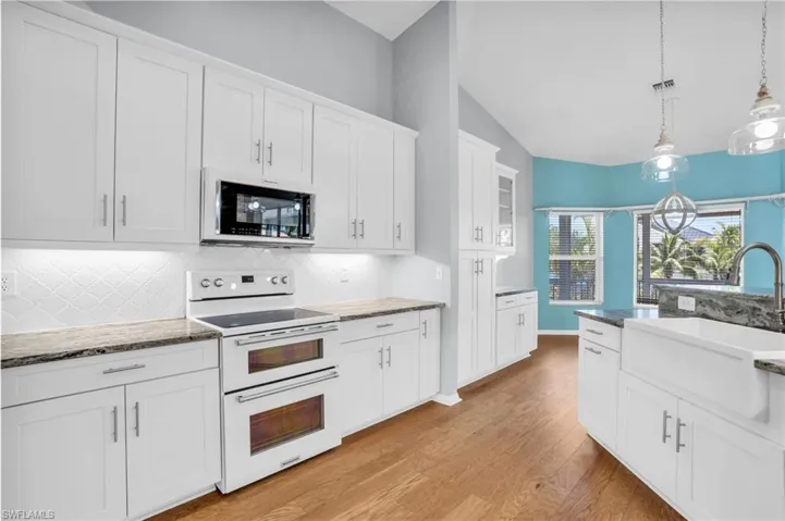 Kitchen featuring decorative backsplash, white cabinets, double oven range, light hardwood / wood-style flooring, and lofted ceiling