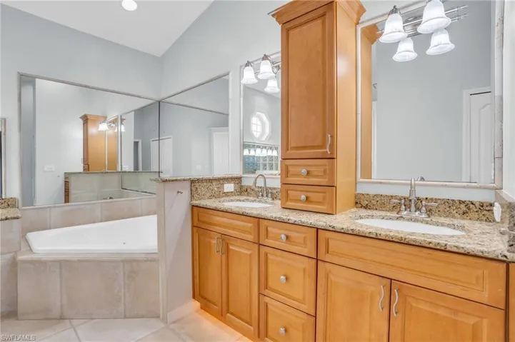 Bathroom with tiled tub, tile patterned floors, and double vanity