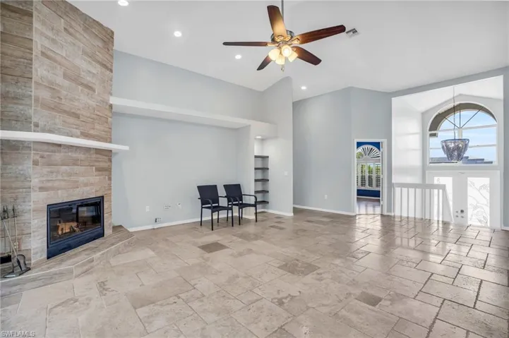 Unfurnished living room featuring a fireplace, french doors, light tile patterned floors, ceiling fan, and a towering ceiling
