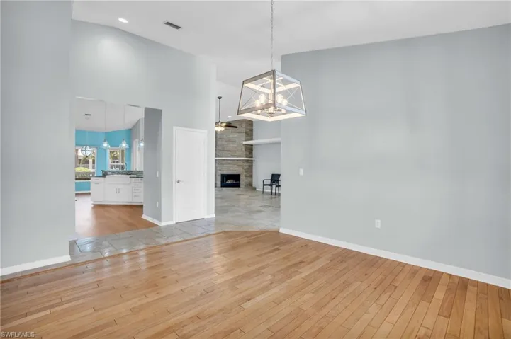 Unfurnished dining area with high vaulted ceiling, a chandelier, light wood-type flooring, and a stone fireplace