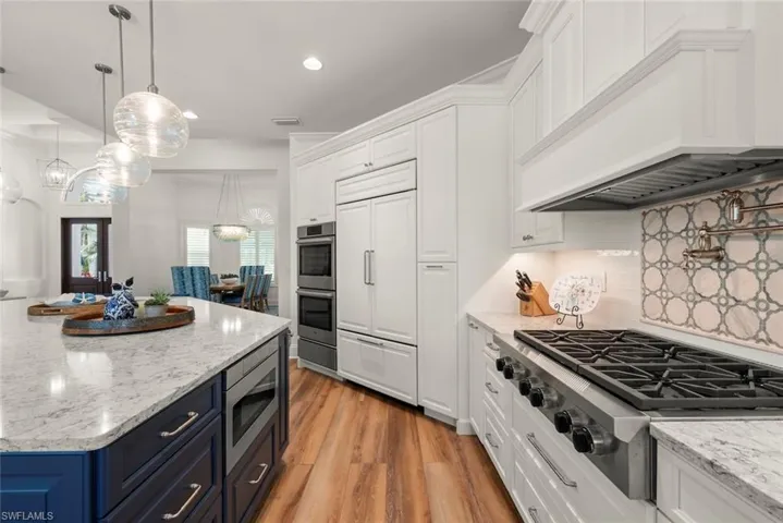 Gourmet kitchen featuring a gas range, a decorative tile backsplash, double wall ovens, a built-in refrigerator, and an island with stone countertops and pendant lighting