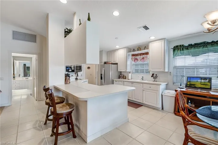 Kitchen with stainless steel appliances, a sink, a kitchen breakfast bar, light countertops, and recessed lighting